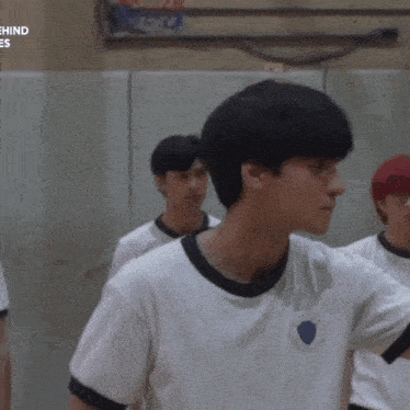 a group of young men are standing in a gym and one of them is wearing a white shirt with a shield on it