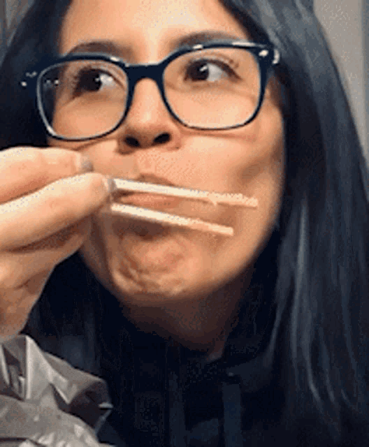 a woman wearing glasses is eating something with chopsticks in her mouth
