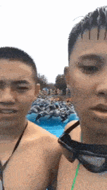two shirtless men wearing goggles are standing next to each other in front of a crowd of people in a pool .