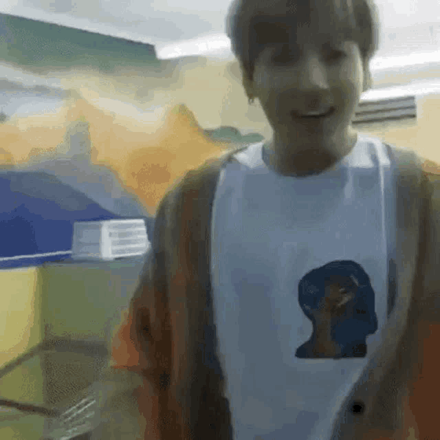 a young man wearing a white t-shirt and a brown cardigan is standing in a room and smiling .