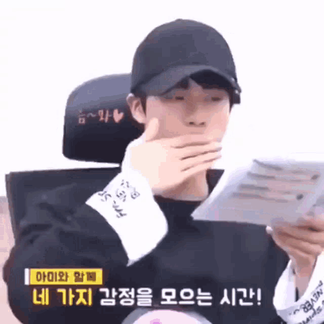 a man wearing a black hat is covering his mouth while holding a piece of paper
