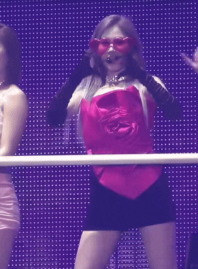 a woman in a pink top and black shorts is standing in front of a purple wall .