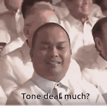 a man is sitting in a crowd of people with his eyes closed and the words `` tone deaf much '' written below him .