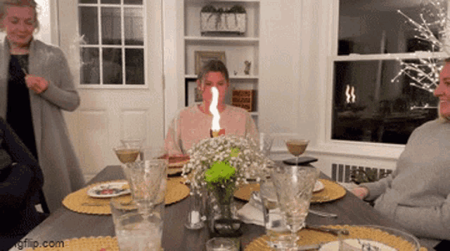 a woman blowing out a candle at a dinner table with a gif.com watermark