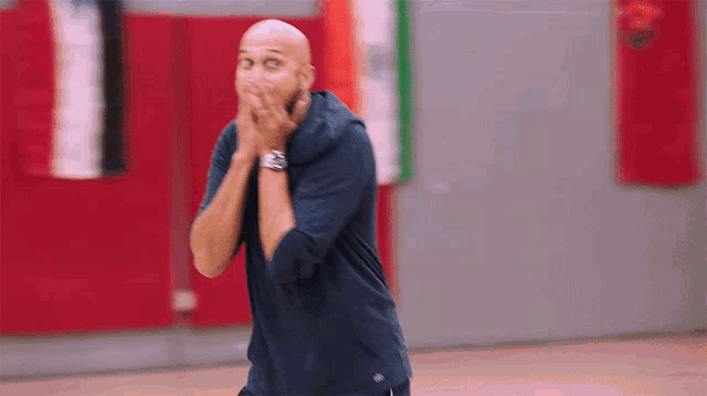 a bald man is covering his mouth with his hands in a gym