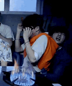a group of people are sitting around a stove and one of them is wearing an orange vest