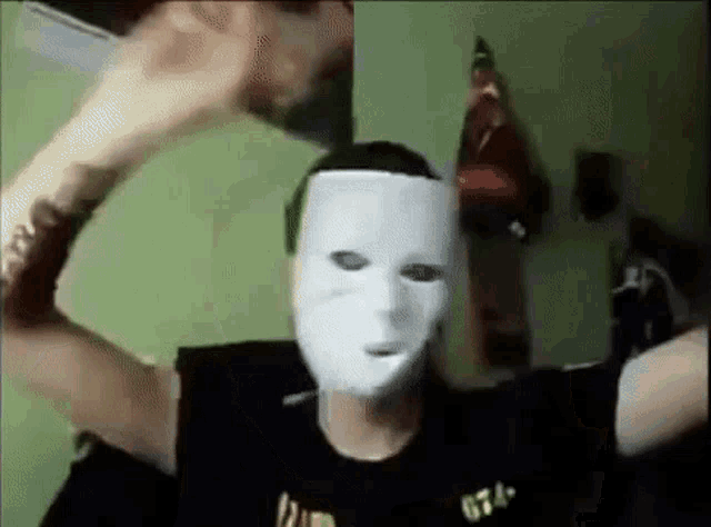 a man wearing a white mask and a black shirt is holding a piece of paper in front of his face .