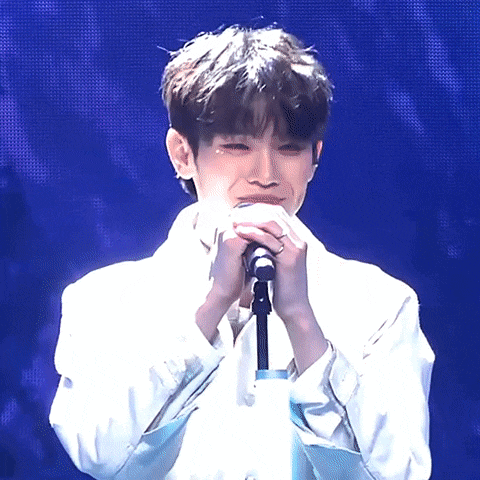 a man in a white shirt is singing into a microphone with his hands on his face