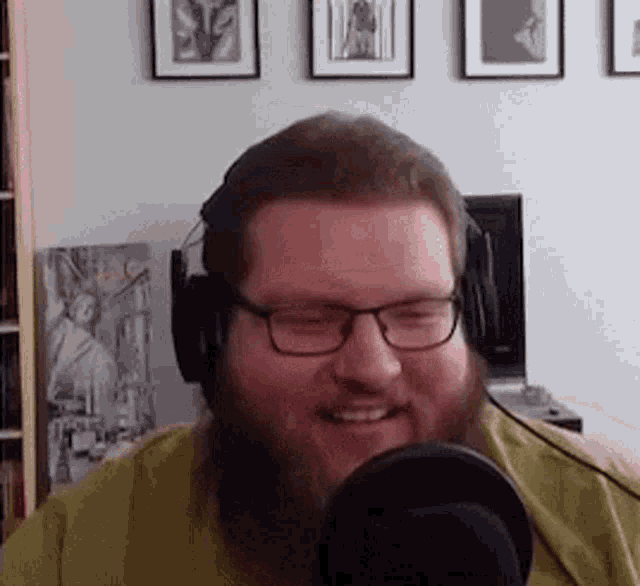 a man with a beard wearing headphones and glasses is smiling into a microphone .