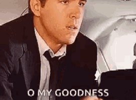 a man in a suit and tie is sitting in the back seat of an airplane and says `` o my goodness '' .