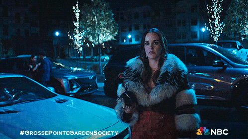 a woman in a fur coat is standing in front of a white car with the nbc logo on the bottom