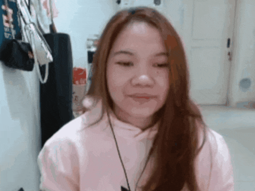 a woman with long red hair is wearing a pink hoodie and smiling .