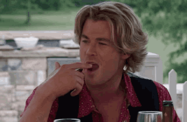 a man with blonde hair is sitting at a table with a glass of wine and a bottle of beer .