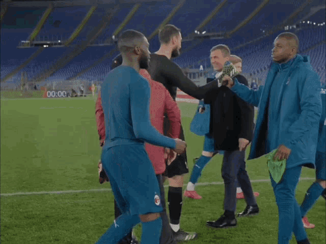 a man in a blue jacket is hugging another man on a soccer field with the words futball karim below him
