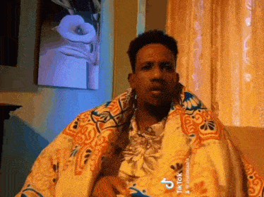 a man wrapped in a blanket is sitting on a couch in a living room .