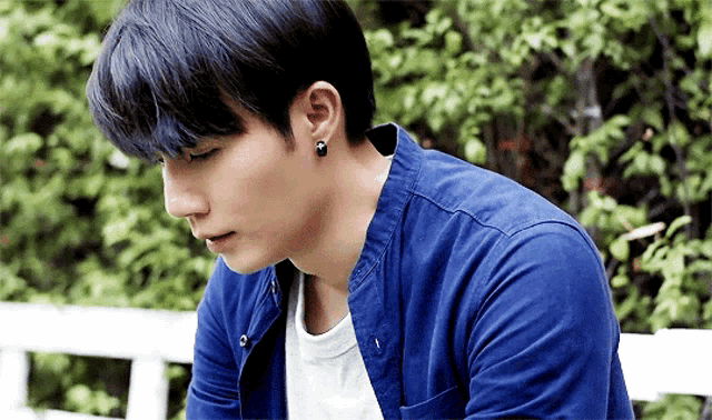 a young man wearing a blue shirt and black earrings