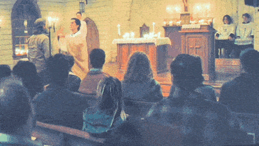 a group of people sitting in a church watching a priest