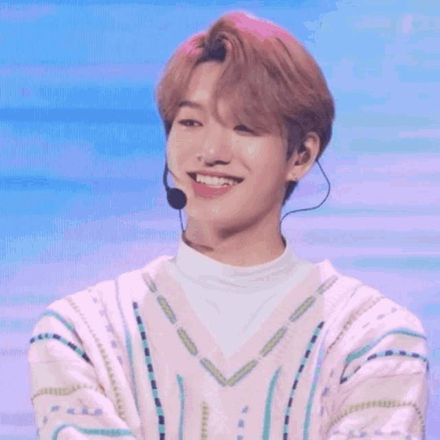 a young man wearing a pink sweater and a white turtleneck smiles with a microphone around his neck .