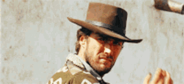 a man wearing a cowboy hat is standing in front of a wall with a gun in his hand
