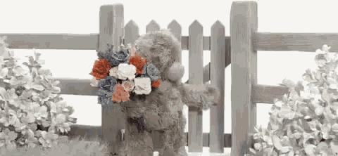 a teddy bear is holding a bouquet of flowers behind a wooden gate .