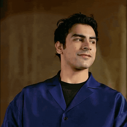 a man in a blue jacket and black shirt looks to his left
