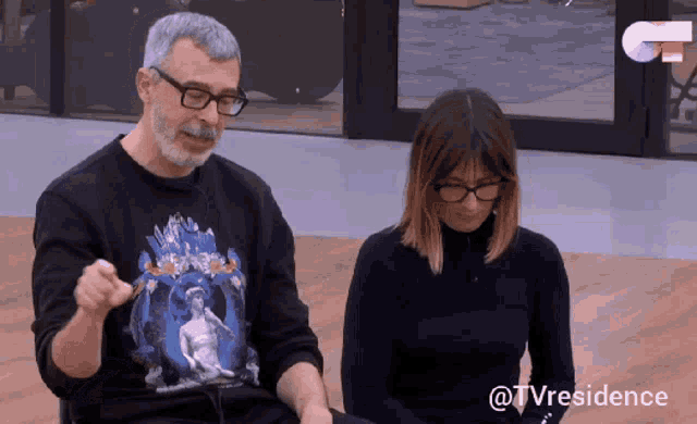 a man and a woman are sitting next to each other and the man is wearing a black shirt with a statue on it