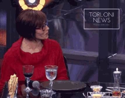 a woman in a red sweater sits at a table with torloni news written on the bottom