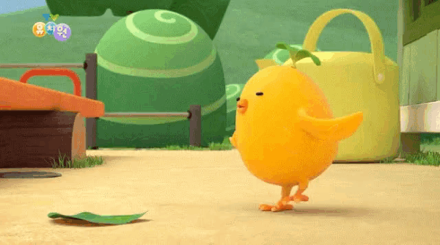a yellow chicken with a green leaf on its head is standing on the ground