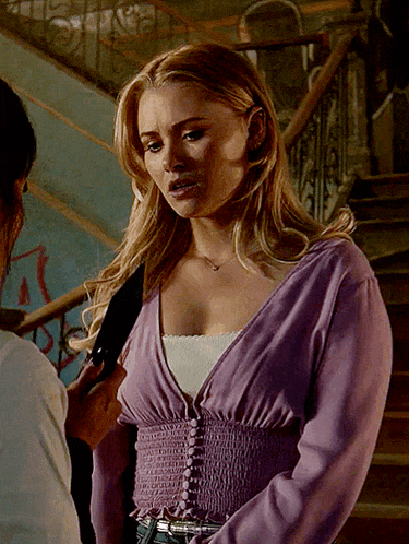 a woman in a purple top stands in front of a staircase with graffiti on it