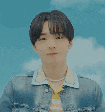a young man wearing a denim jacket and a pearl necklace is making a peace sign .