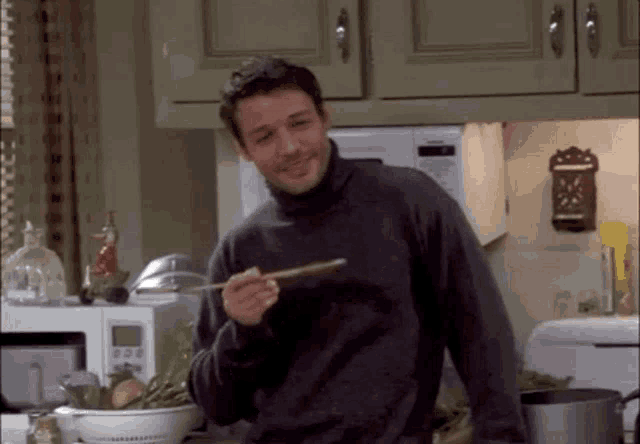 a man in a turtleneck sweater is holding a spoon in his hand