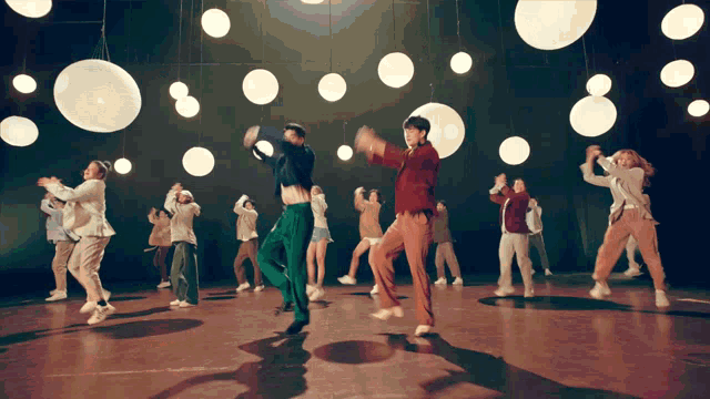 a group of young people are dancing in a dark room with lights hanging from the ceiling