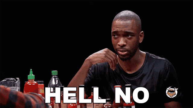 a man is sitting at a table with bottles of hot sauce and says hell no