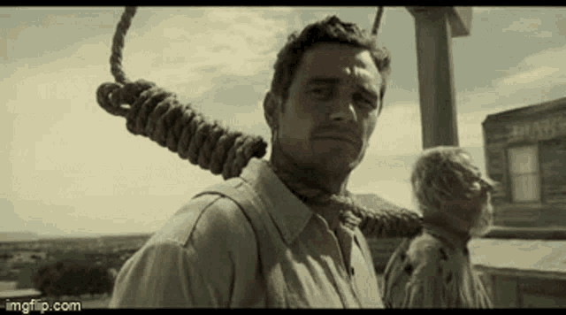 a man with a rope around his neck is standing in front of a building .