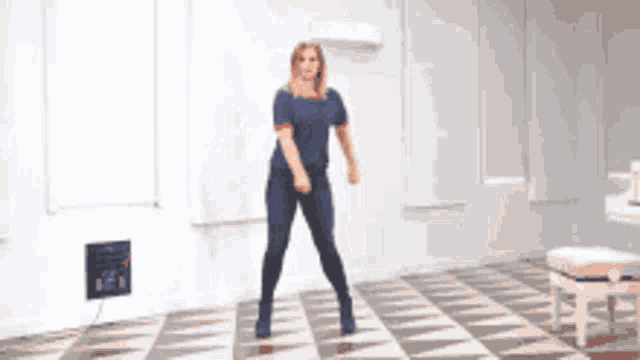 a woman in a blue shirt is dancing on a checkered floor