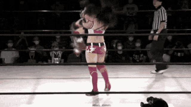 two women are wrestling in a ring with a referee standing behind them