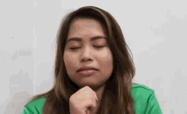 a woman in a green shirt is making a funny face with her eyes closed and her hand on her chin .