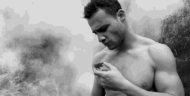 a black and white photo of a shirtless man holding a butterfly in his hand .