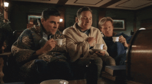 three men sitting on a couch drinking tea