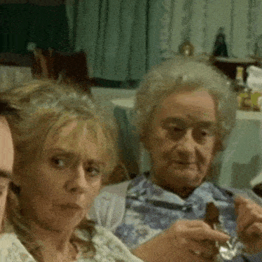 two older women are sitting at a table with a man . one of the women is holding a knife and fork .