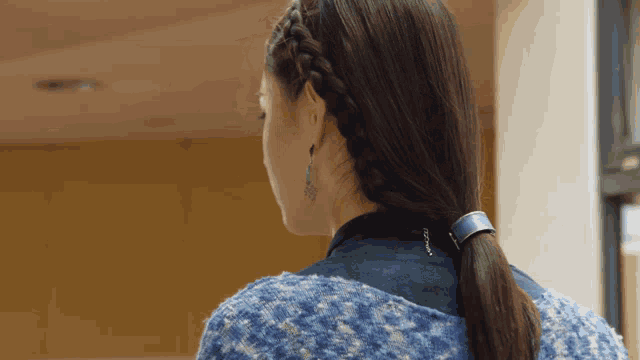 a woman wearing a braided ponytail and earrings is looking over her shoulder