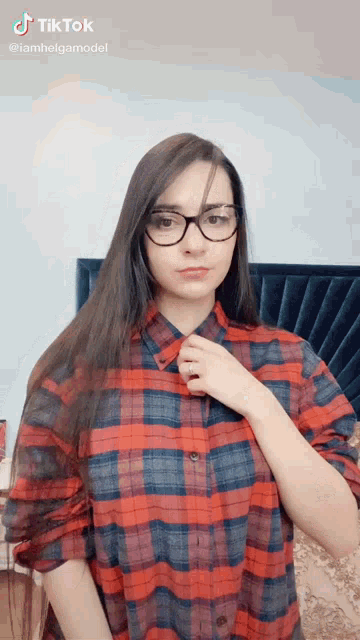 a woman wearing glasses and a plaid shirt is standing in front of a blue headboard .