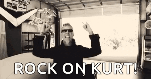 a man is standing in a garage with his arms outstretched and a sign that says `` rock on kurt '' .