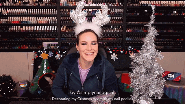 a woman wearing a reindeer headband is talking about decorating her christmas tree with her nail polish