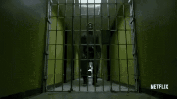a man is standing behind bars in a jail cell in a hallway .
