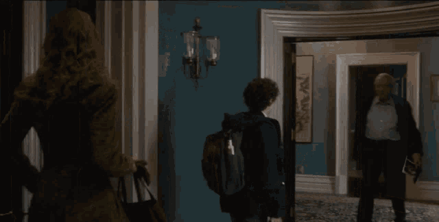a man in a suit stands in a hallway looking at a woman and a boy with a backpack