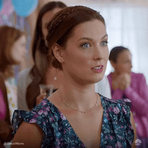 a woman in a floral dress and necklace is standing in a crowd of people at a party .