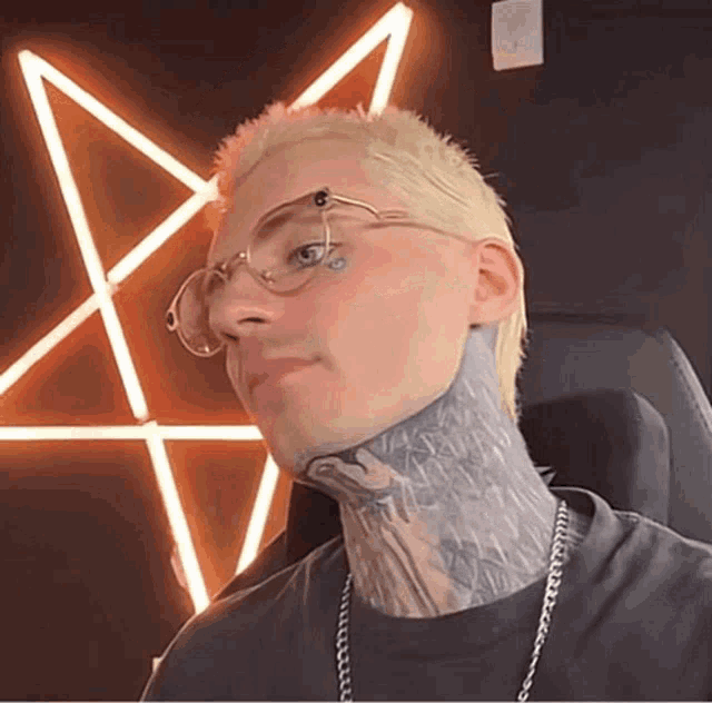 a man with glasses and a tattoo on his neck looks at the camera