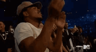 a man in a hat is clapping his hands in a crowd of people .