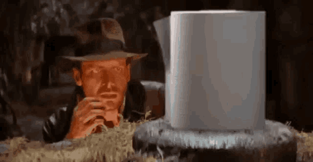 a man wearing a hat is looking at a roll of toilet paper